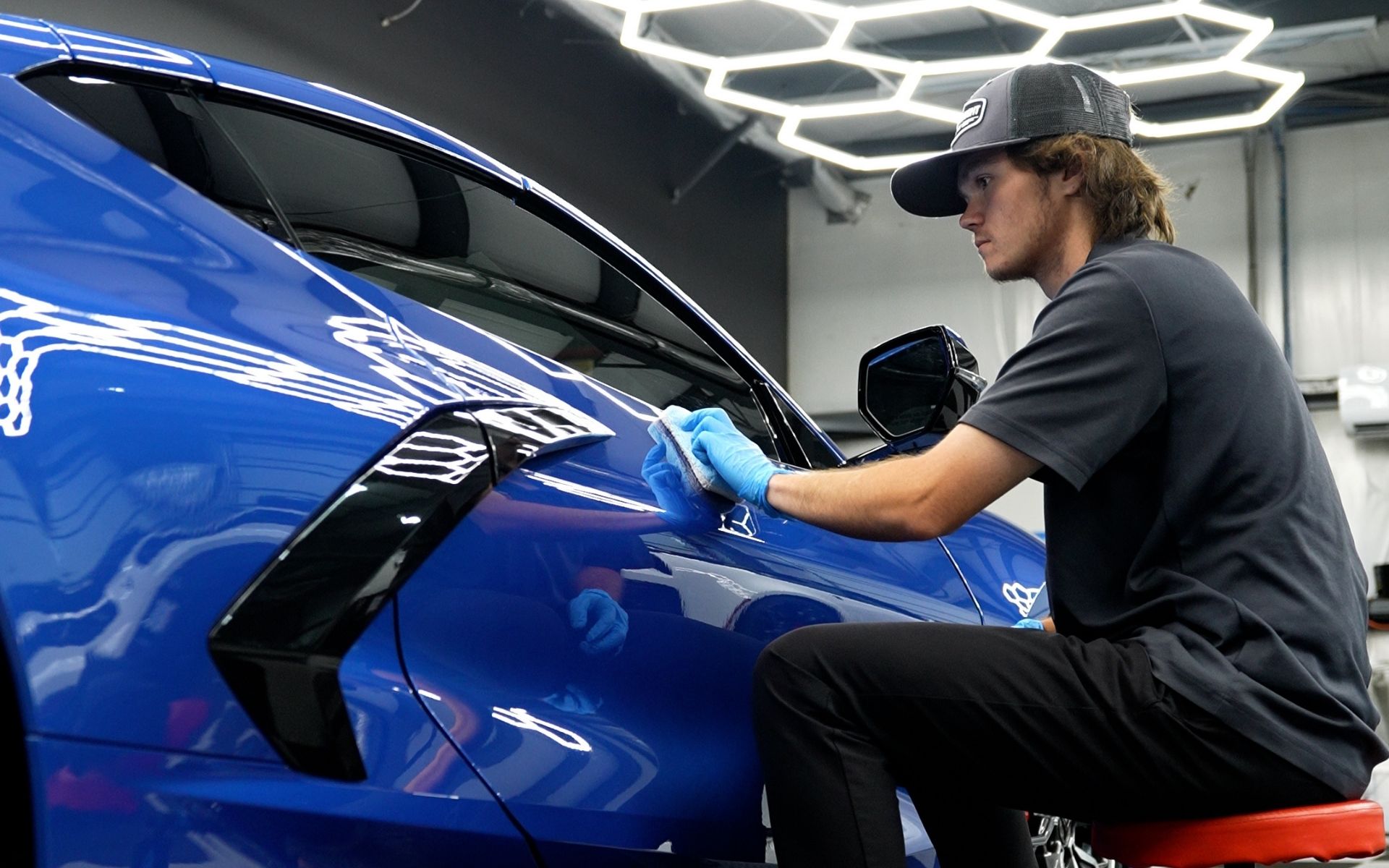 Technician applying ceramic coating to a blue car fender at NVS Customs window tinting & car wrap shop in Wilmington, NC