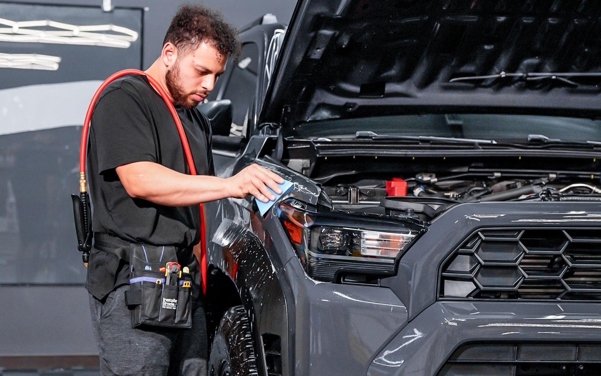 Installer applying clear paint protection film (clear bra) to the front end of a vehicle in the NVS Customs shop.